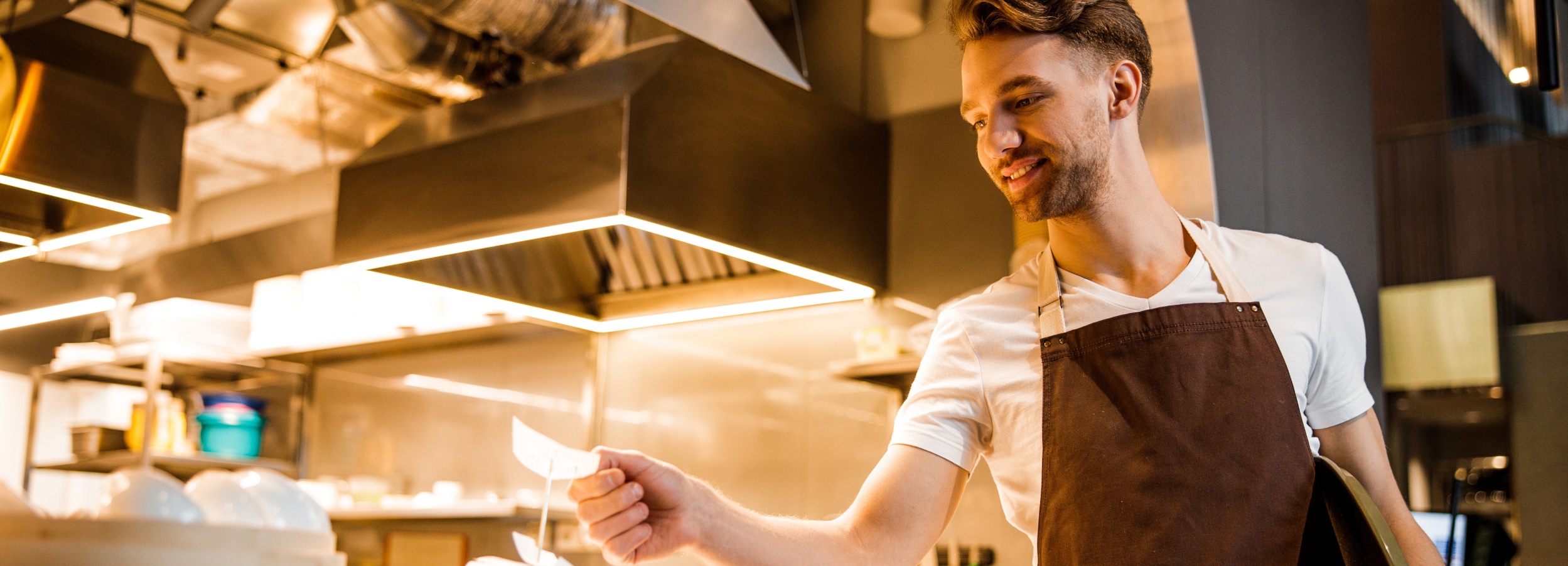 Junger Kellner wartet neben der Küche auf die nächste Bestellung und legt einen Bestellzettel ab.
