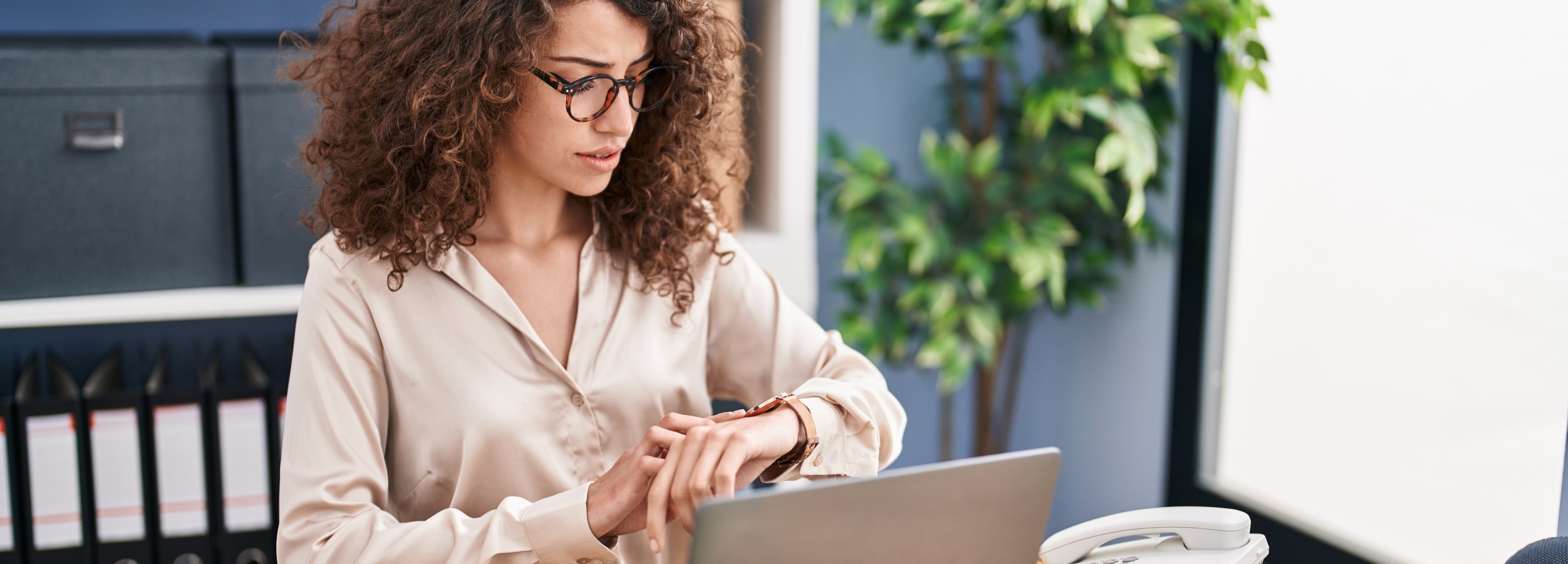 Geschäftsfrau arbeitet am Laptop im Büro und schaut auf die Uhr.